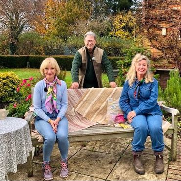 Esther and Jane Horrocks are sat on a bench with Alan Titchmarsh standing behind them and the bench.