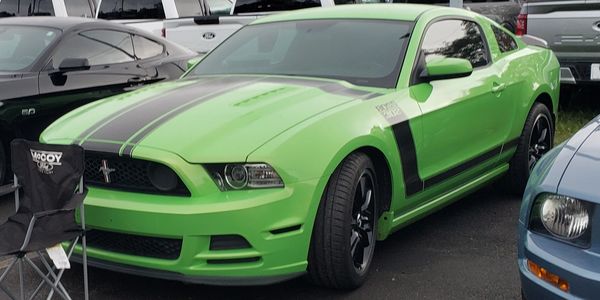 Bright green Ford Mustang with black racing stripes parked among other cars.