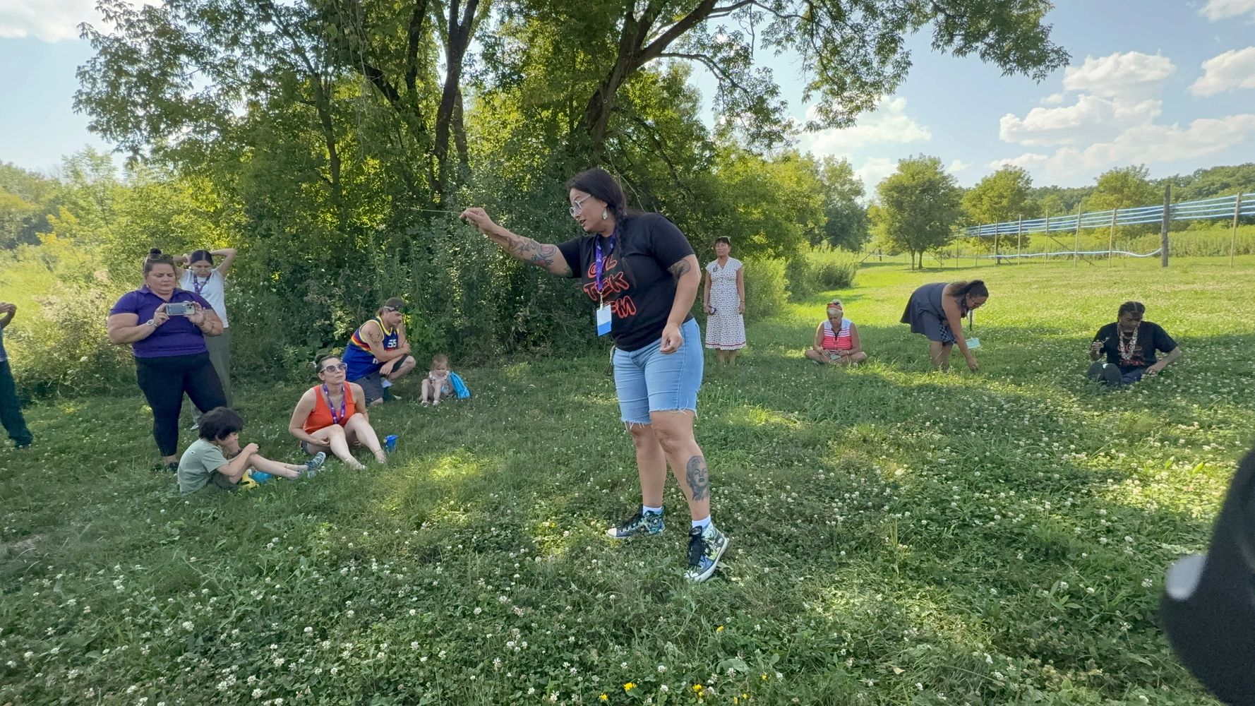Group outdoors learning about nature in a grassy field under trees on a sunny day.