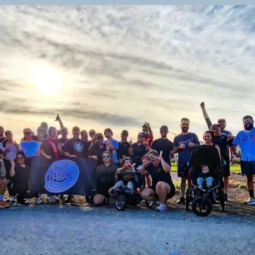 Large group posing outdoors with a banner under a bright sky.