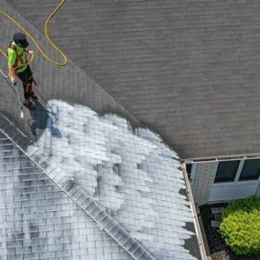 Worker pressure washing a roof.