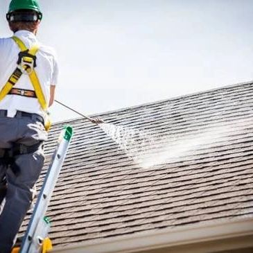 Person pressure washing a shingled roof.