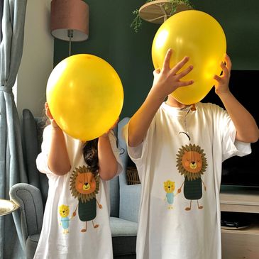 Two young children holding ballons and wearing t-shirts withBaba Lion and Little Lion