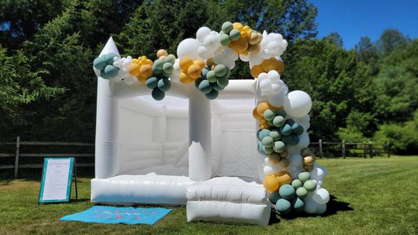 White bounce castle with slide combo with green white and gold balloon garland