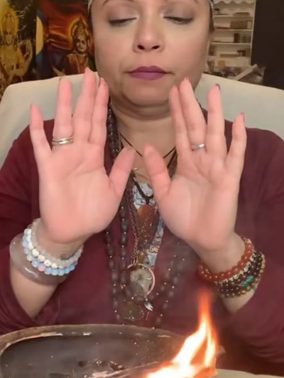 Person performing a ritual with hands over a fire, wearing bracelets and rings.