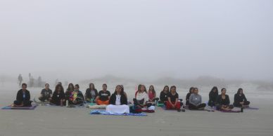 Group of people meditating on a foggy beach.