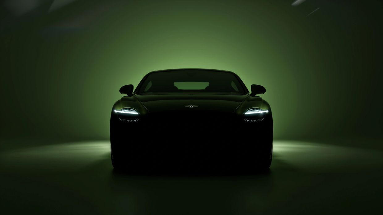 Front view of a sleek Bentley car with headlights on against a green backdrop.