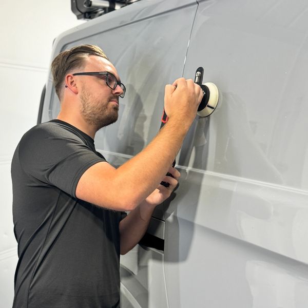Man polishing a gray van with a power buffer.