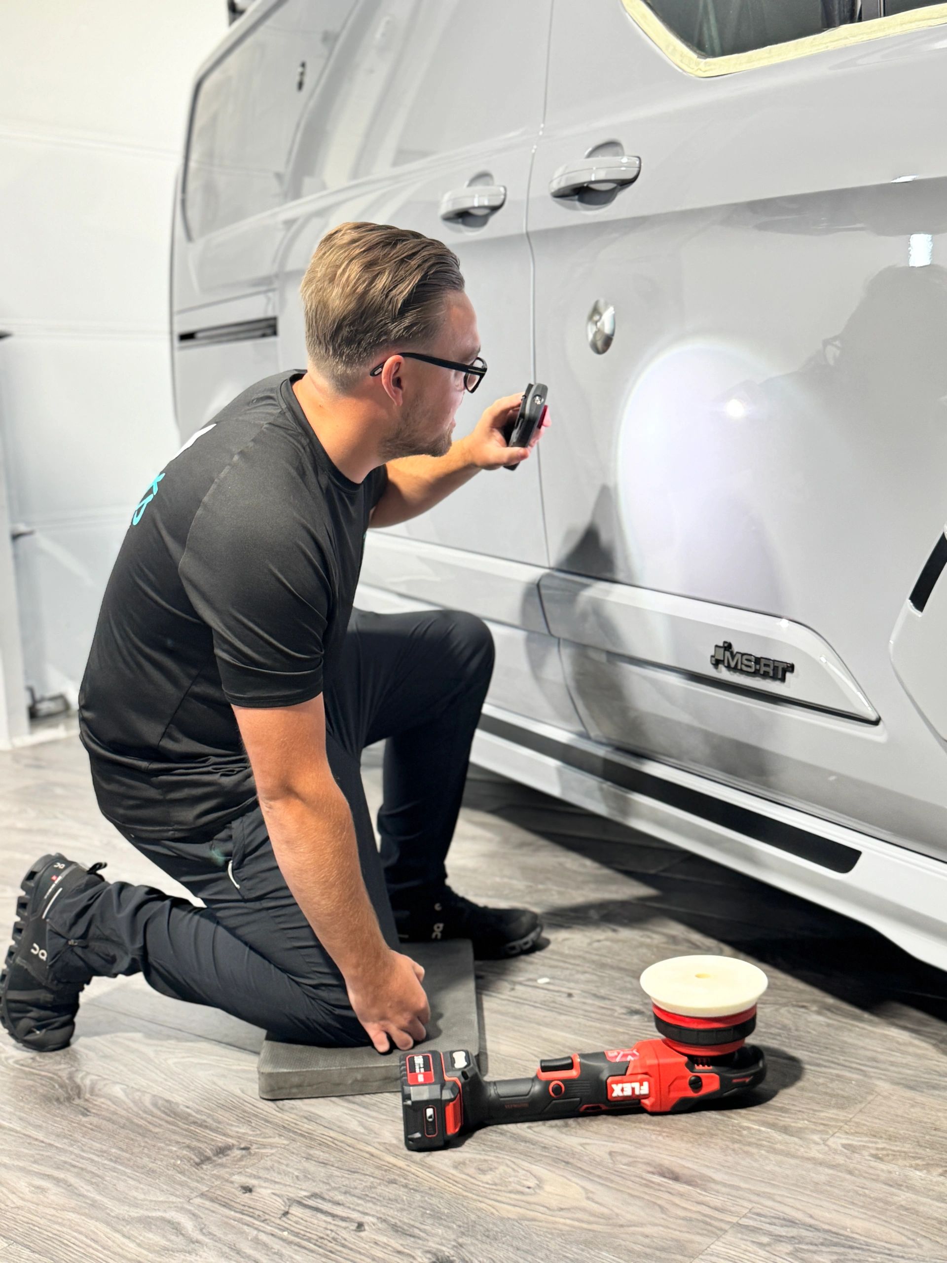 Man inspecting damage on a white vehicle's side panel indoors.