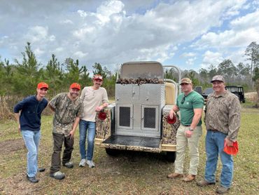 Five men posing behind a hunting vehicle with game birds on a cloudy day.