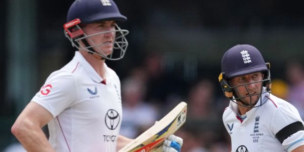 Two cricket players in white uniforms and helmets.