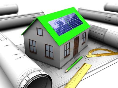 Model house with solar panels on green roof surrounded by architectural plans and tools.