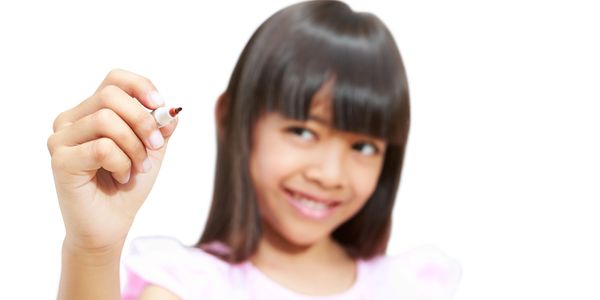 Girl smiling and holding a pencil up as if she's about to write on a board.