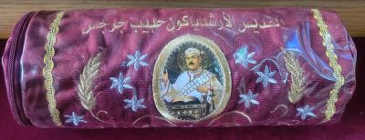 Decorative maroon fabric with embroidered portrait and Arabic script.