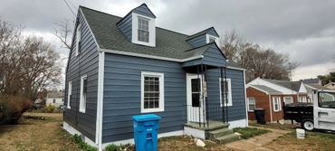 Blue house with white trim and a small front porch under a cloudy sky.