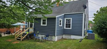 Cozy backyard with blue house, small patio, and outdoor seating under trees.