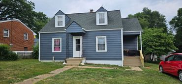 Blue house with white trim, pink curtains, and a red car parked outside.