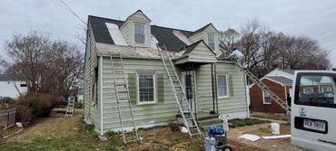 A house undergoing roof repairs with ladders and a worker on the roof.