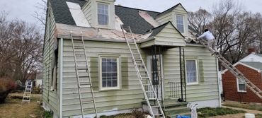 House undergoing roof repair with ladders and a worker on the roof.