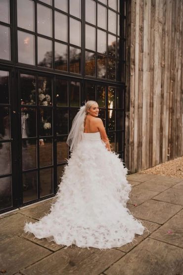 Bride in a feathered wedding dress smiling over her shoulder.