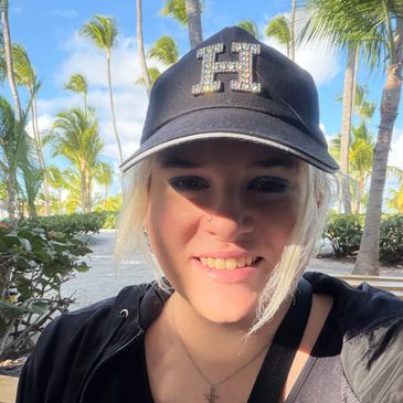 Smiling woman in a black hat outdoors with palm trees.