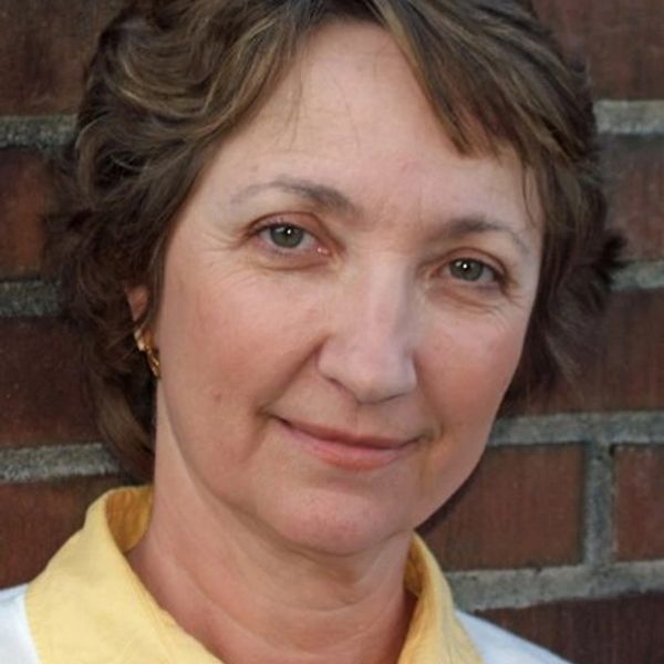 Middle-aged woman smiling gently with brick wall background.