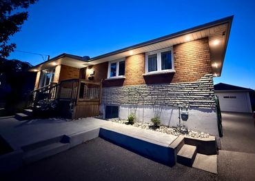 Well-lit suburban brick house exterior at dusk with a driveway and garage.