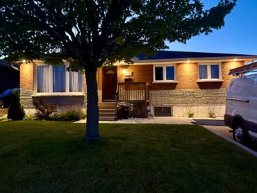 Evening view of a cozy brick house with warm porch lights and a tree in the front yard.