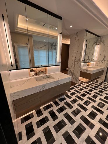 Modern bathroom with marble counters and patterned black and white tile floor.