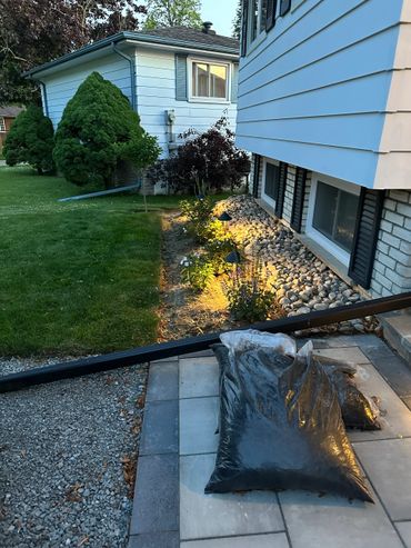 Backyard garden at dusk with illuminated plants and bags of soil on a tiled patio.