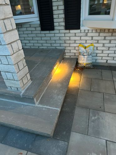 Stone steps with built-in yellow lights next to a brick wall and patio.