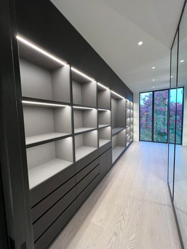 Modern walk-in closet with sleek black shelves, drawers, and natural light.