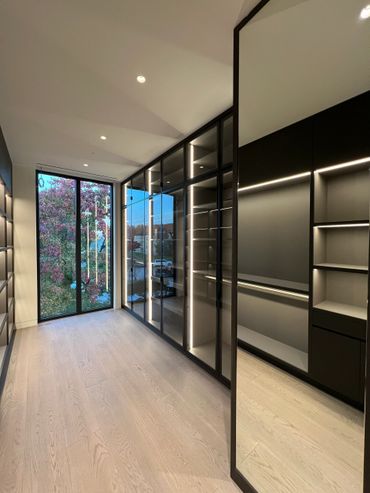 Modern walk-in closet with glass doors and integrated lighting.