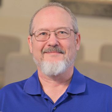 Smiling middle-aged man with glasses and a beard in a blue shirt.