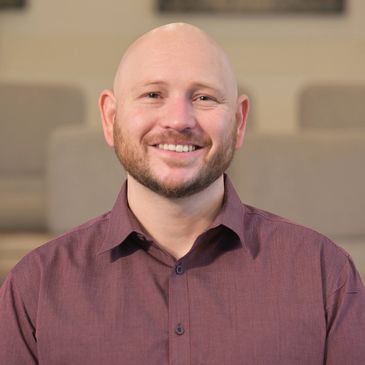 Smiling bald man in a maroon shirt seated indoors.