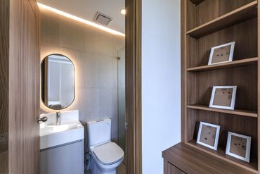 Modern bathroom with backlit mirror and wooden shelving unit with framed art.