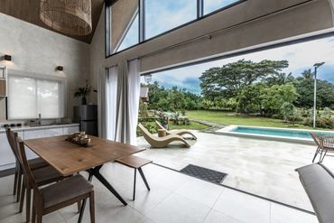 Modern dining area opens to a spacious patio with a pool and garden view.