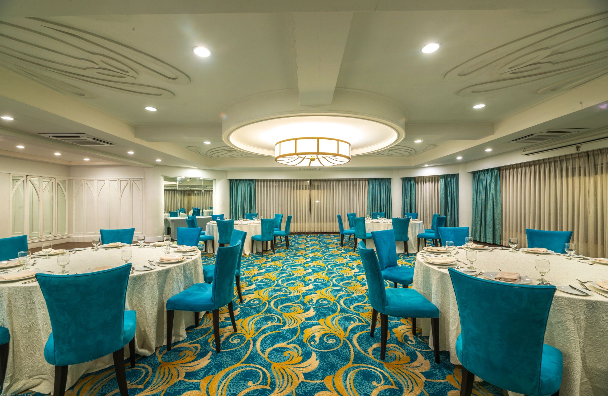 Elegant dining room with teal chairs and ornate carpet.