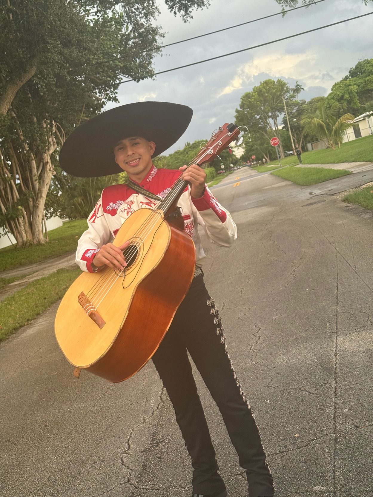 Young man in traditional mariachi attire playing a guitar on a street.