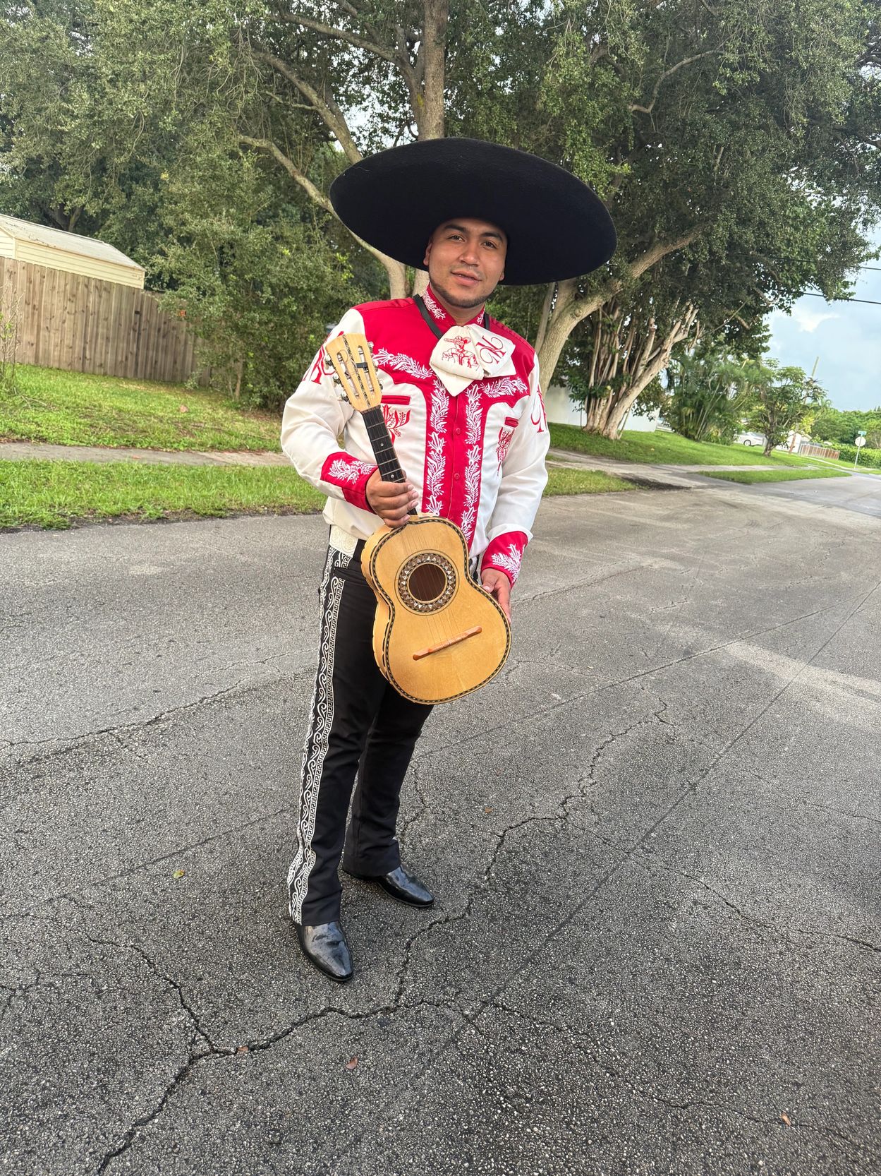 Man in traditional mariachi attire holding a guitar on a street.