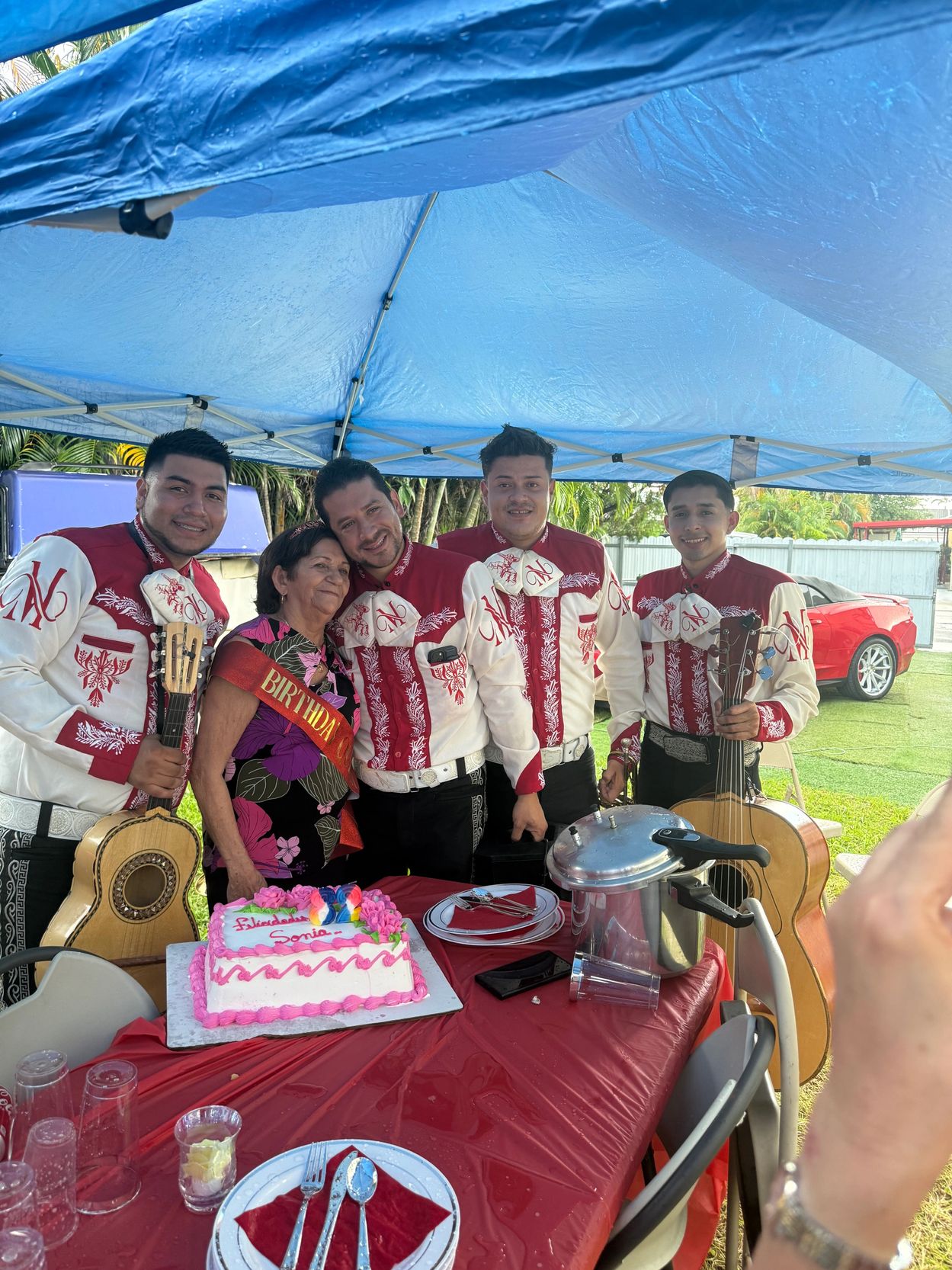 A birthday celebration with a mariachi band and a decorated cake outdoors.