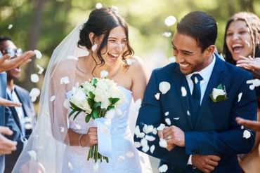 Joyful bride and groom laughing as flower petals are thrown at their wedding.