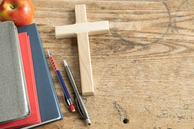 Wood cross with stack of books and apple and pens on wood desk
