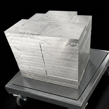 Stack of shiny metal blocks on a wheeled platform against a black background.