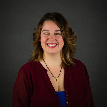 Smiling woman with shoulder-length hair and a maroon blouse against a dark background.