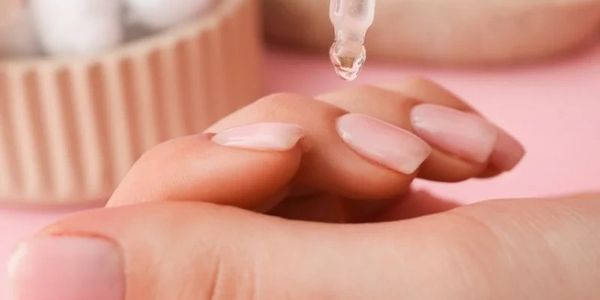 Close-up of a hand receiving a drop of oil or serum on manicured nails.