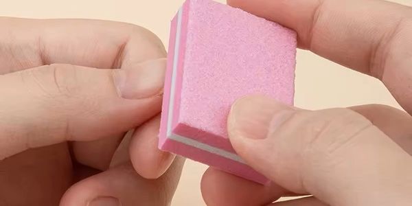 Close-up of hands holding a small pink sanding sponge.