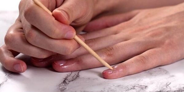 A person cleaning under fingernails with a wooden stick.