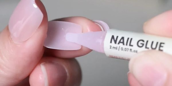 Applying nail glue to a false nail tip for manicure.