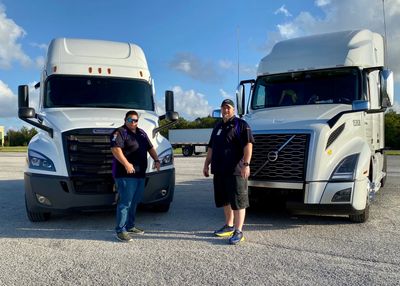 Two people in front of two white trucks